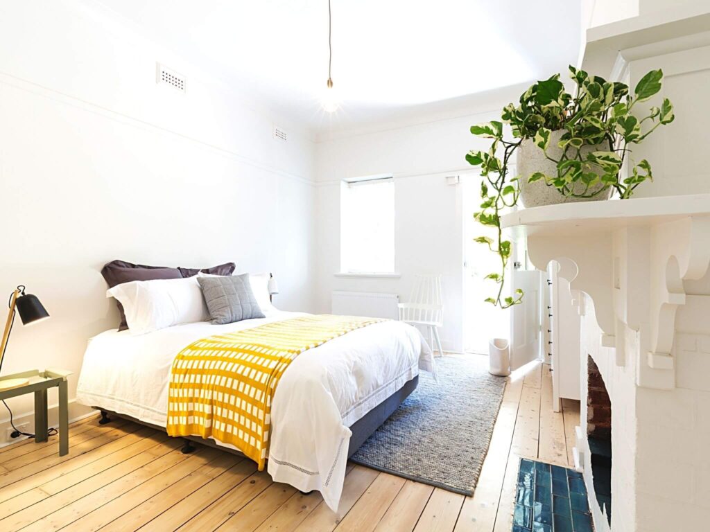 Cozy guest room inspiration. A white room with wooden flooring, a white fireplace and a double bed with white and yellow bedding. 